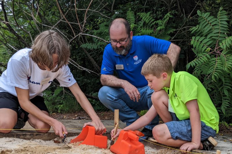 A UWG professor helps children attending summer camp dig