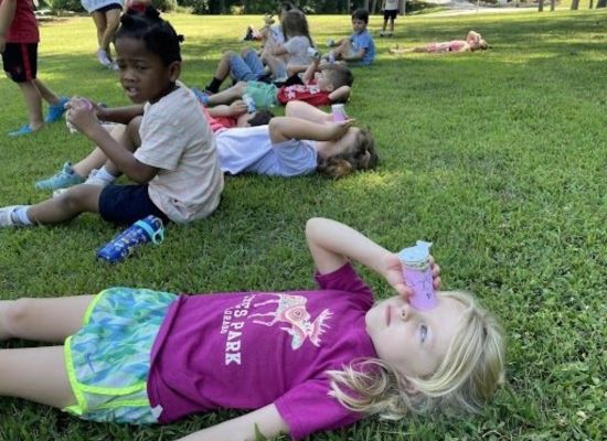A child lays on the ground and looks through a tube at the sky at a UWG summer camp