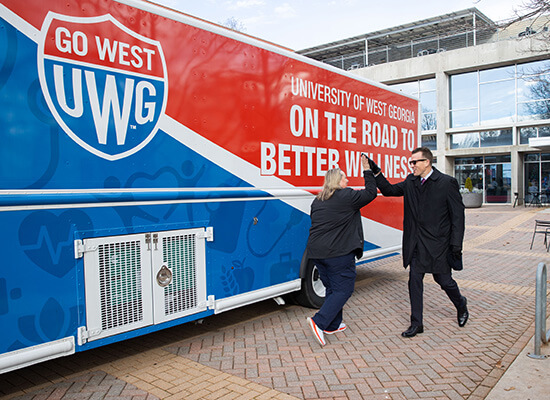 UWG President Brendan Kelly high fives Chief Wellness Officer Bridgette Stewart in front of UWG's mobile health unit.