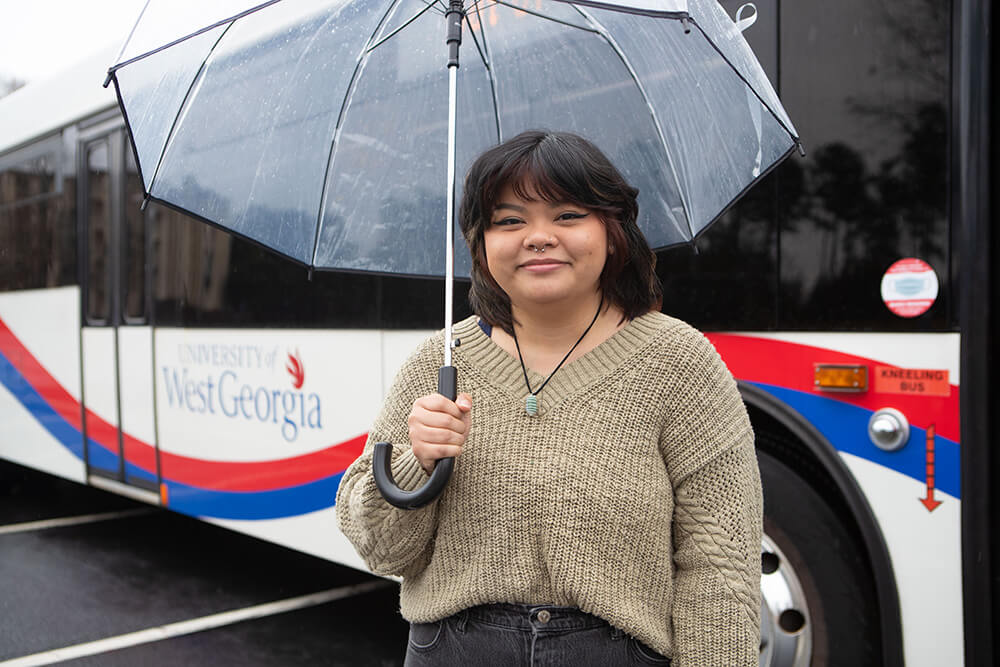 Nancy Vu in front of a bus holding an umbrella