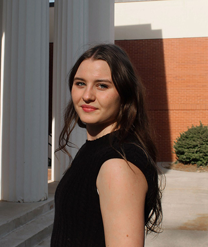 Hoegger poses for a portrait in a black shirt while looking over her shoulder at the camera