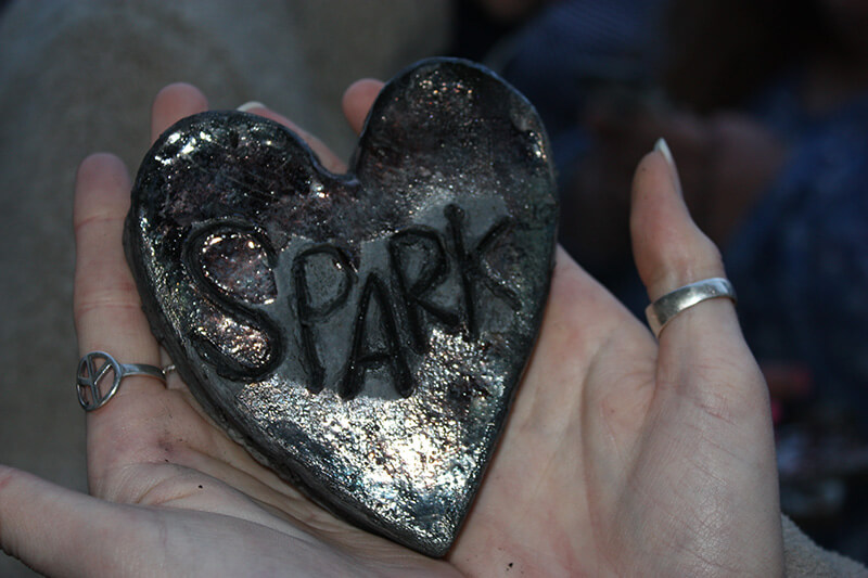 open palms holding a heart-shaped rock with "Spark" written on it