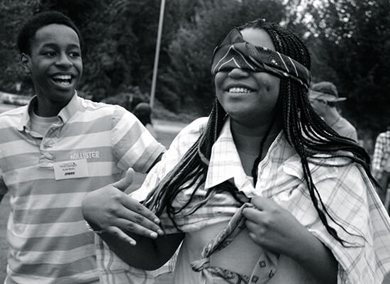 a laughing blindfolded teen being guided by her peers