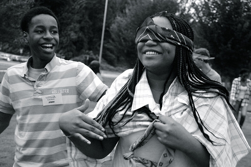 laughing blindfolded teenager being led by a peer 