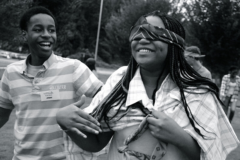 laughing blindfolded teenager being led by a peer