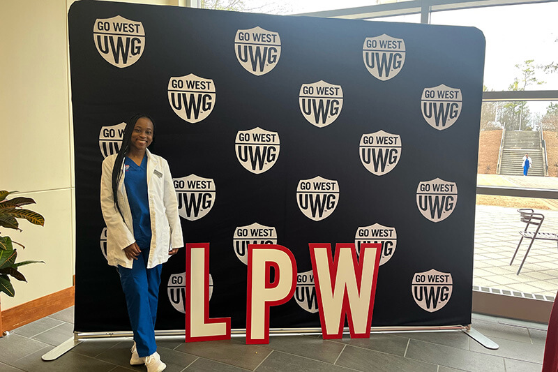 UWG nursing student in front of a Go West backdrop that has the letters LPW