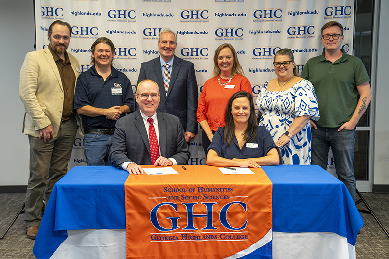 Georgia Highlands College and University of West Georgia faculty and staff members pose for a photo at a table with a Georgia Highlands College tablecloth