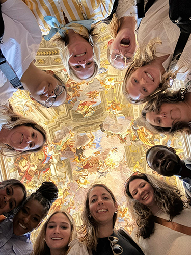 Group of nursing students and faculty looking down with museum ceiling in the background.