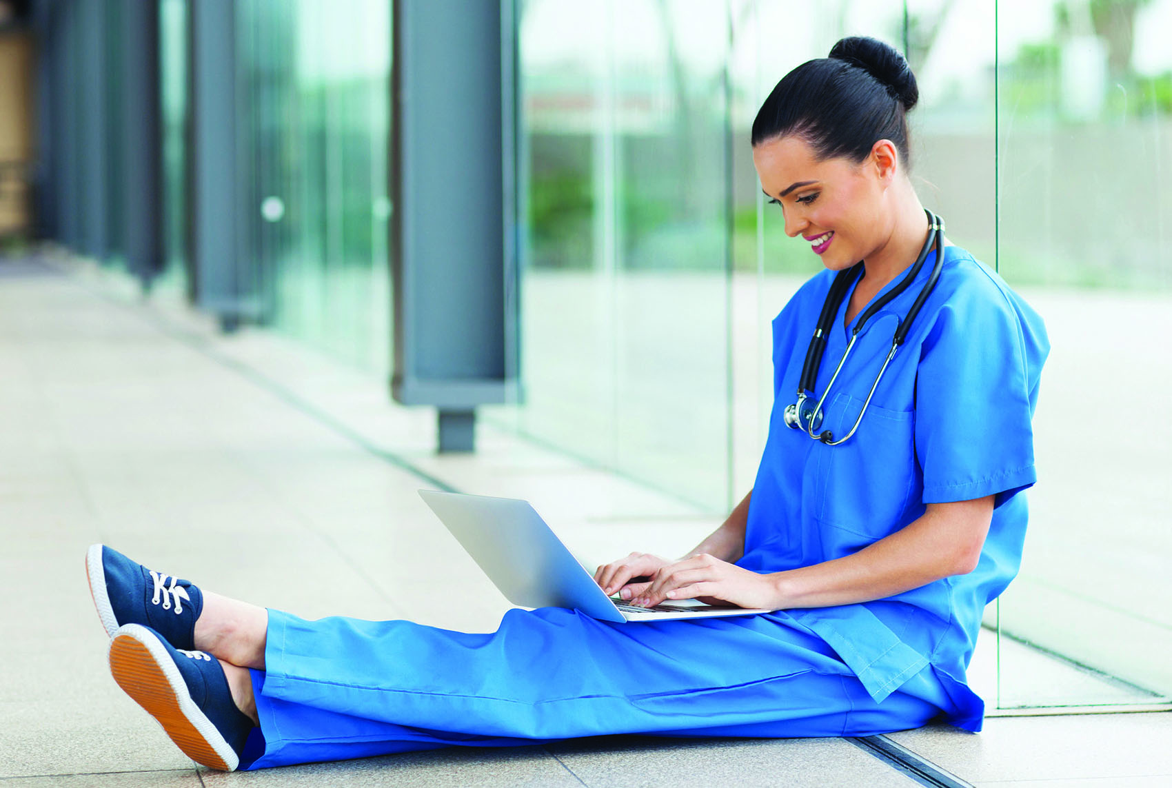 Nursing student sitting on the floor working on her laptop.