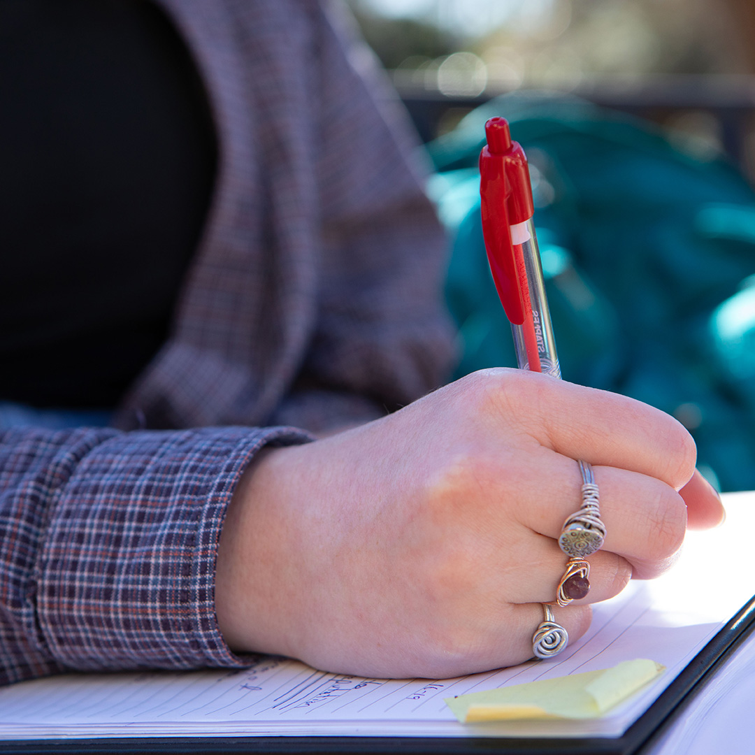 student writing on a notepad outside