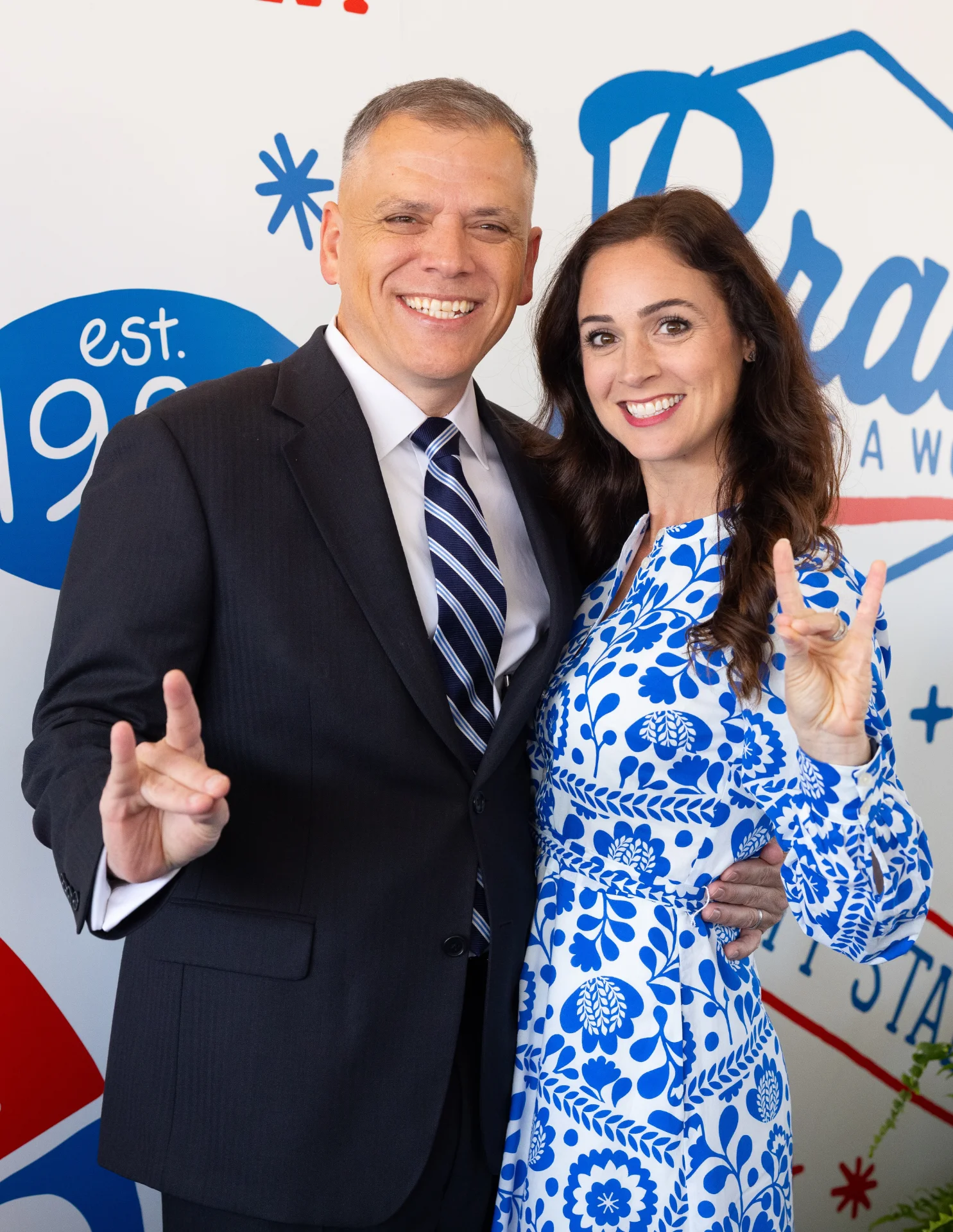 President Johnson and First Lady standing in front of UWG banner holding up the wolf hand sign.