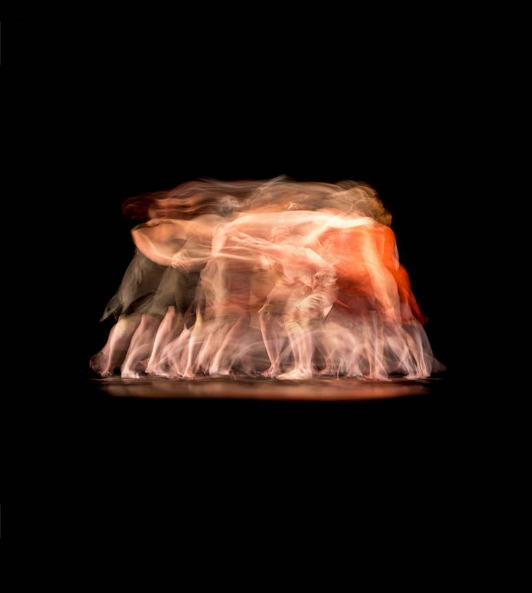 abstract long-exposure image of multiple overlapping human forms moving close together against a black background