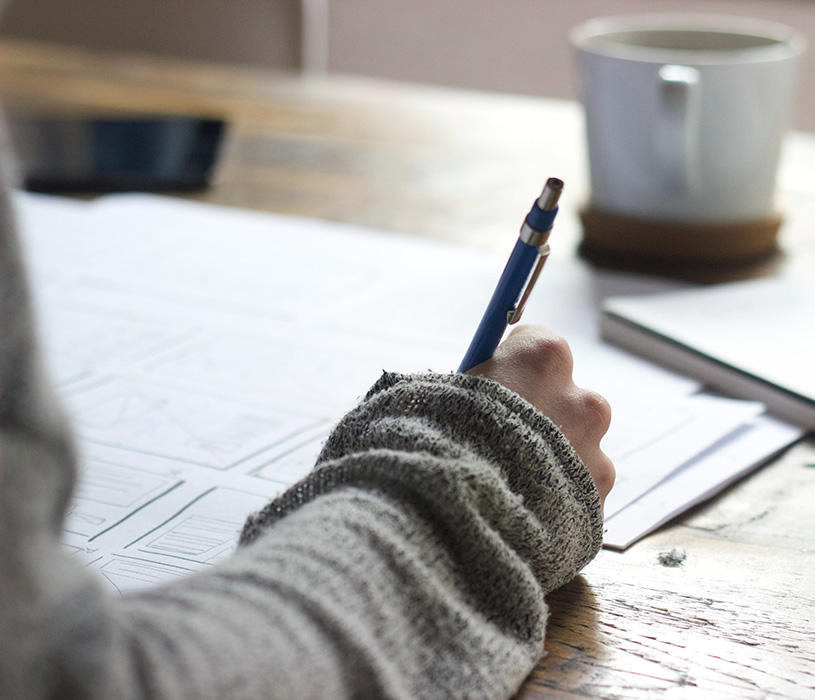 person's hand writing on table with coffee cup