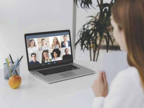 Woman sitting at laptop open to 8 individuals in a zoom-like setup.