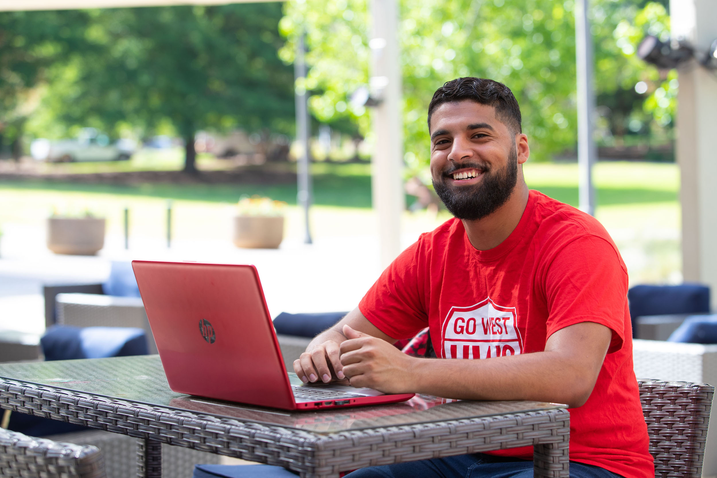 Male student smiling outside with red laptop.