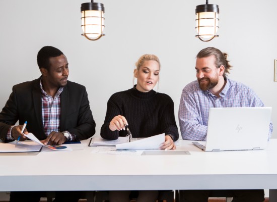 three people working at a desk, going over documents