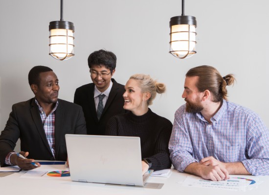 four business students conversing while viewing a laptop