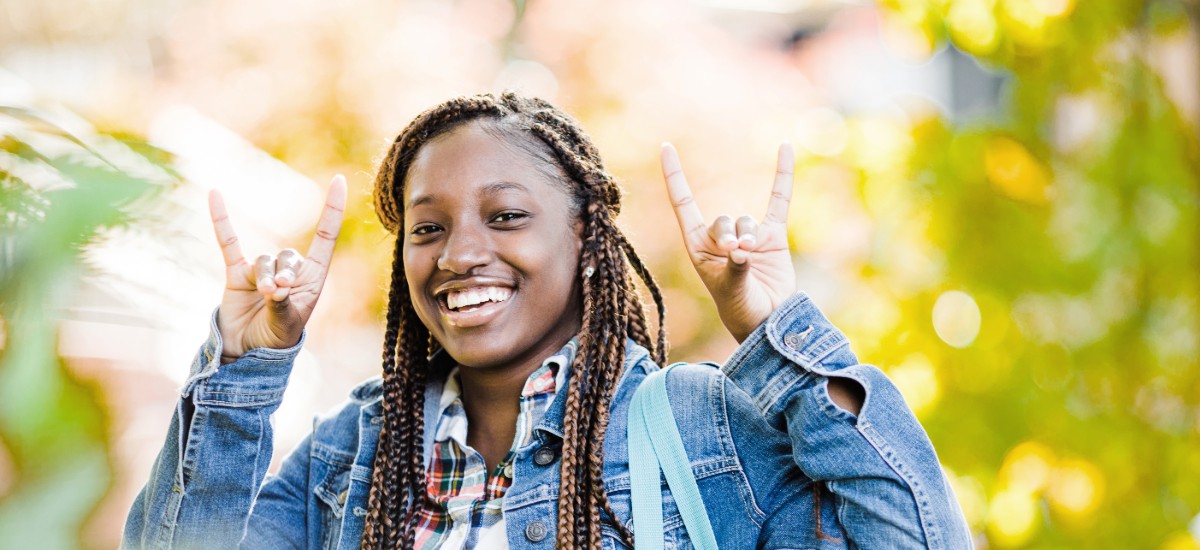 Female student smiling outside holding up the wolf hand sign.