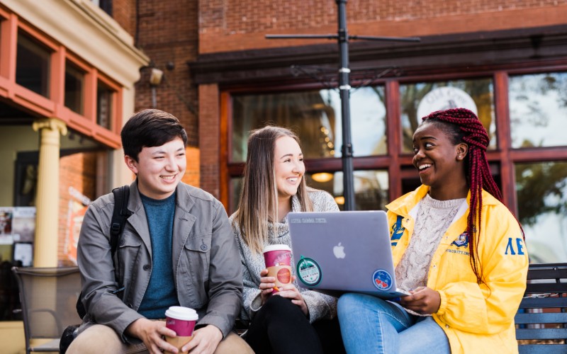 three students chatting and studying on the laptop in front of cafe 