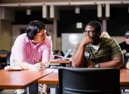 two students discussing academics in a large classroom