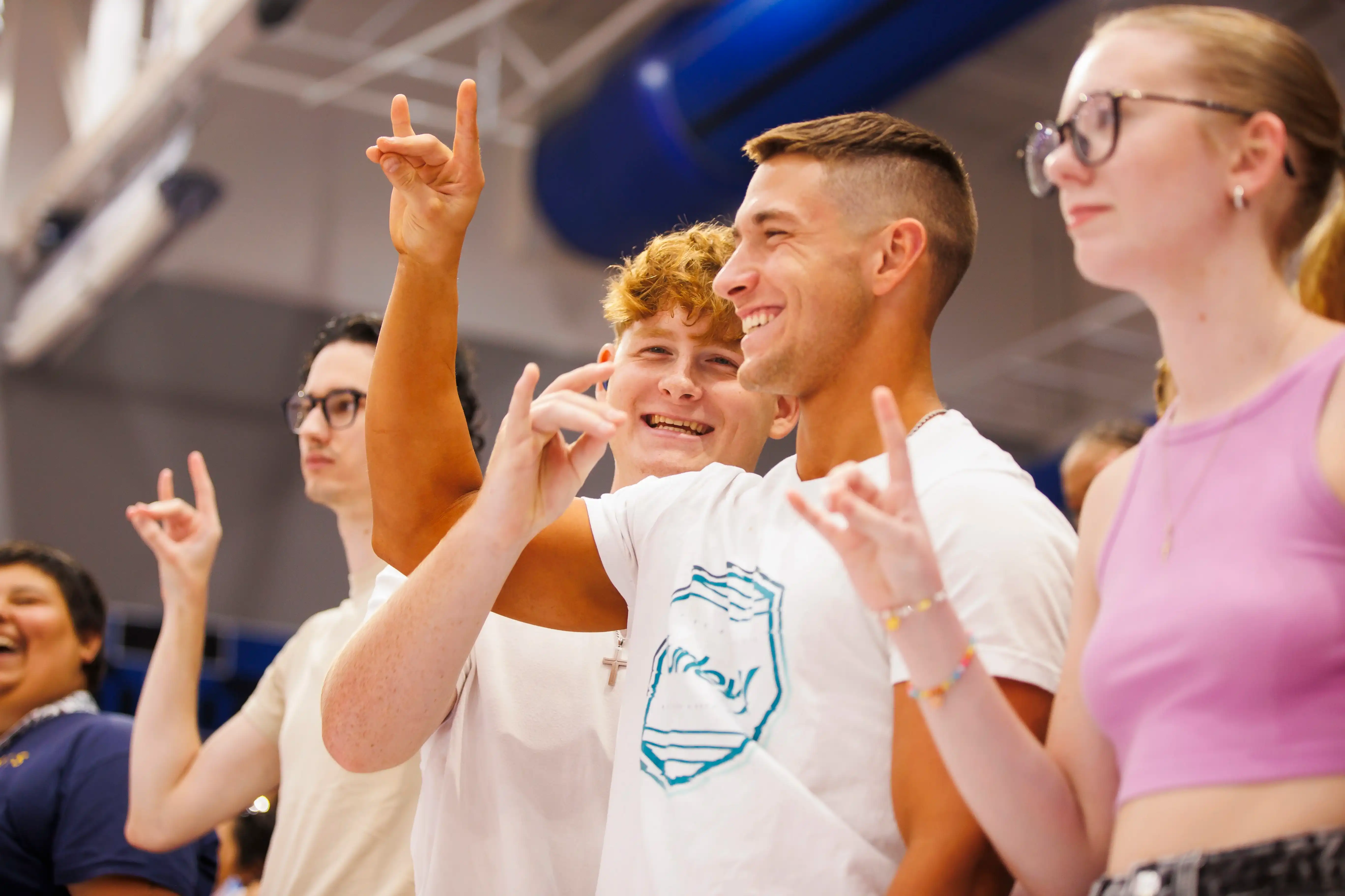 Students together in the Coliseum holding up the wolf hand sign.