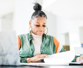 Female student studying with notes and laptop.