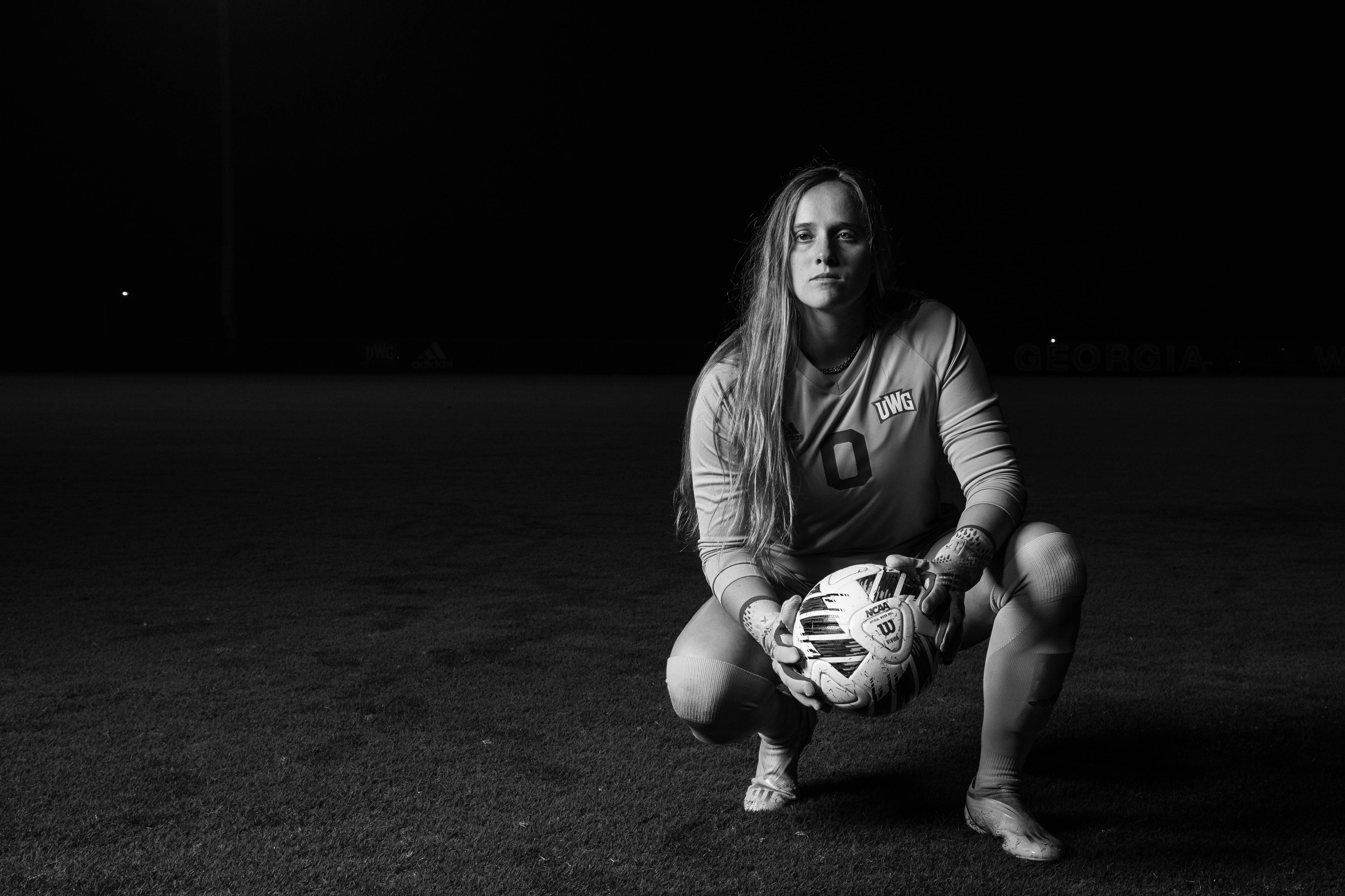 UWG Women's Soccer player kneeling on the field holding a soccer ball. 