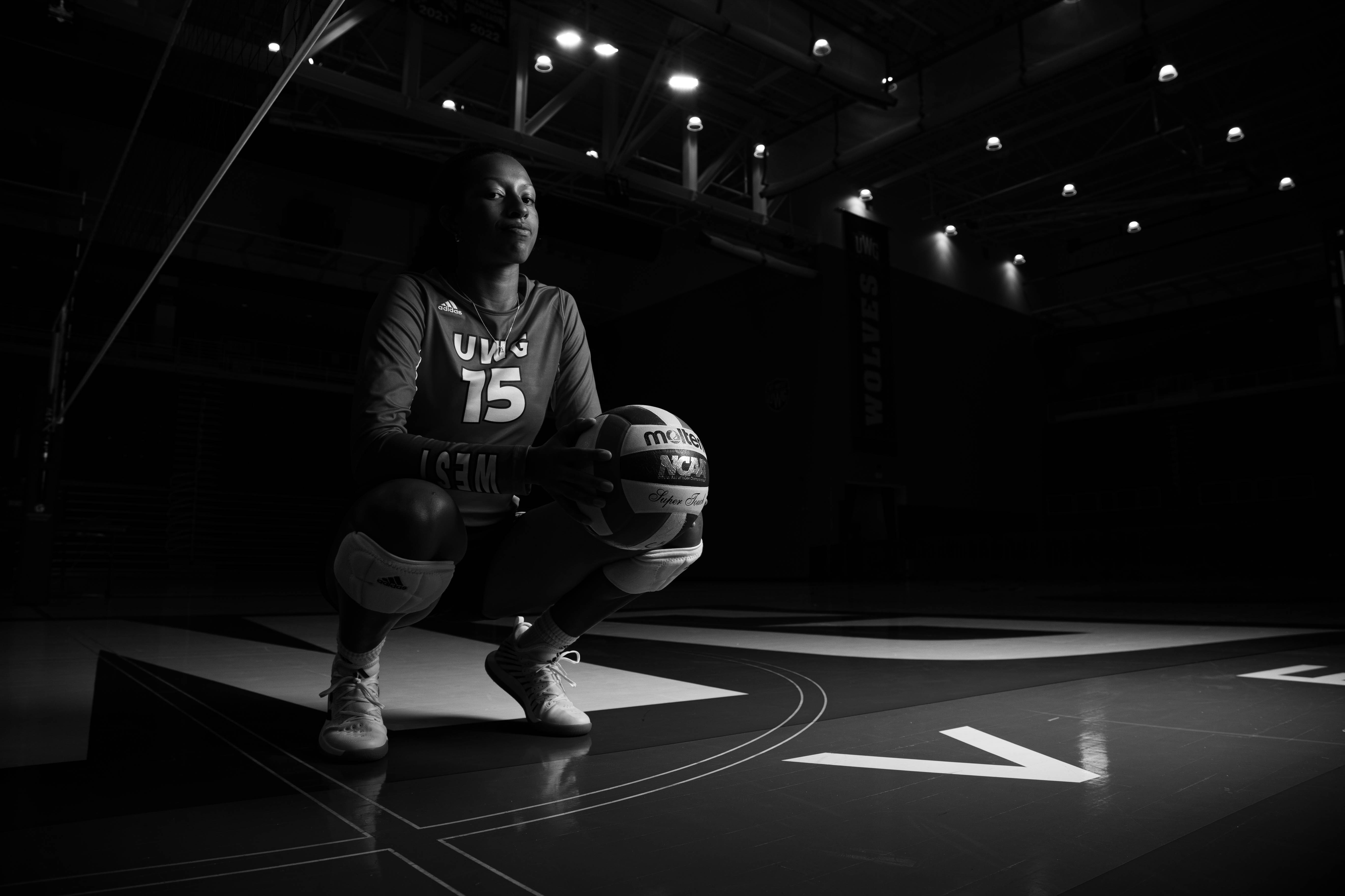 Volleyball player squatting on the court holding a volleyball.