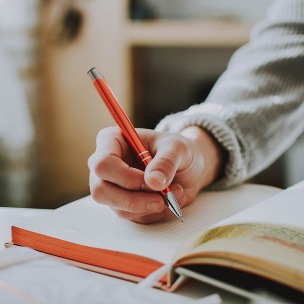 Persons hand writing notes in a notebook.