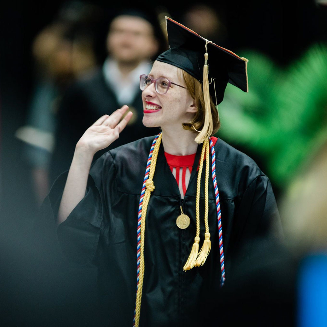 Photo of Sadie walking at graduation; she's waving at the crowd