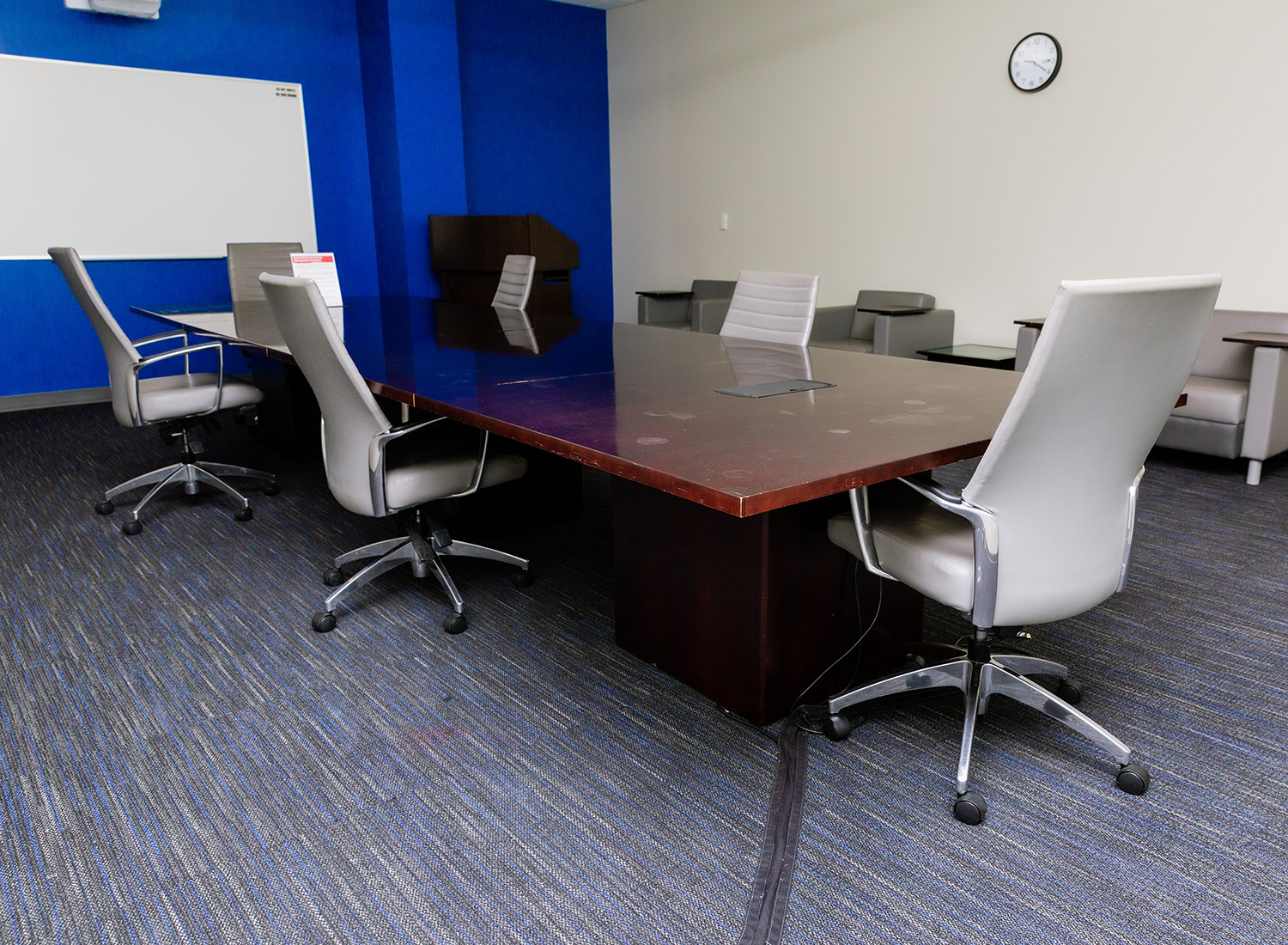 Conference Room 105 view facing right showcasing a conference table with chairs, a podium, and a whiteboarad