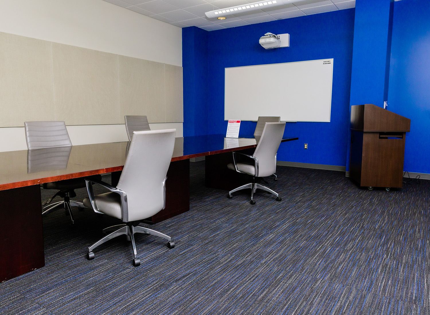 Conference Room 105 view facing left showcasing a conference table with chairs, a podium, and a whiteboarad