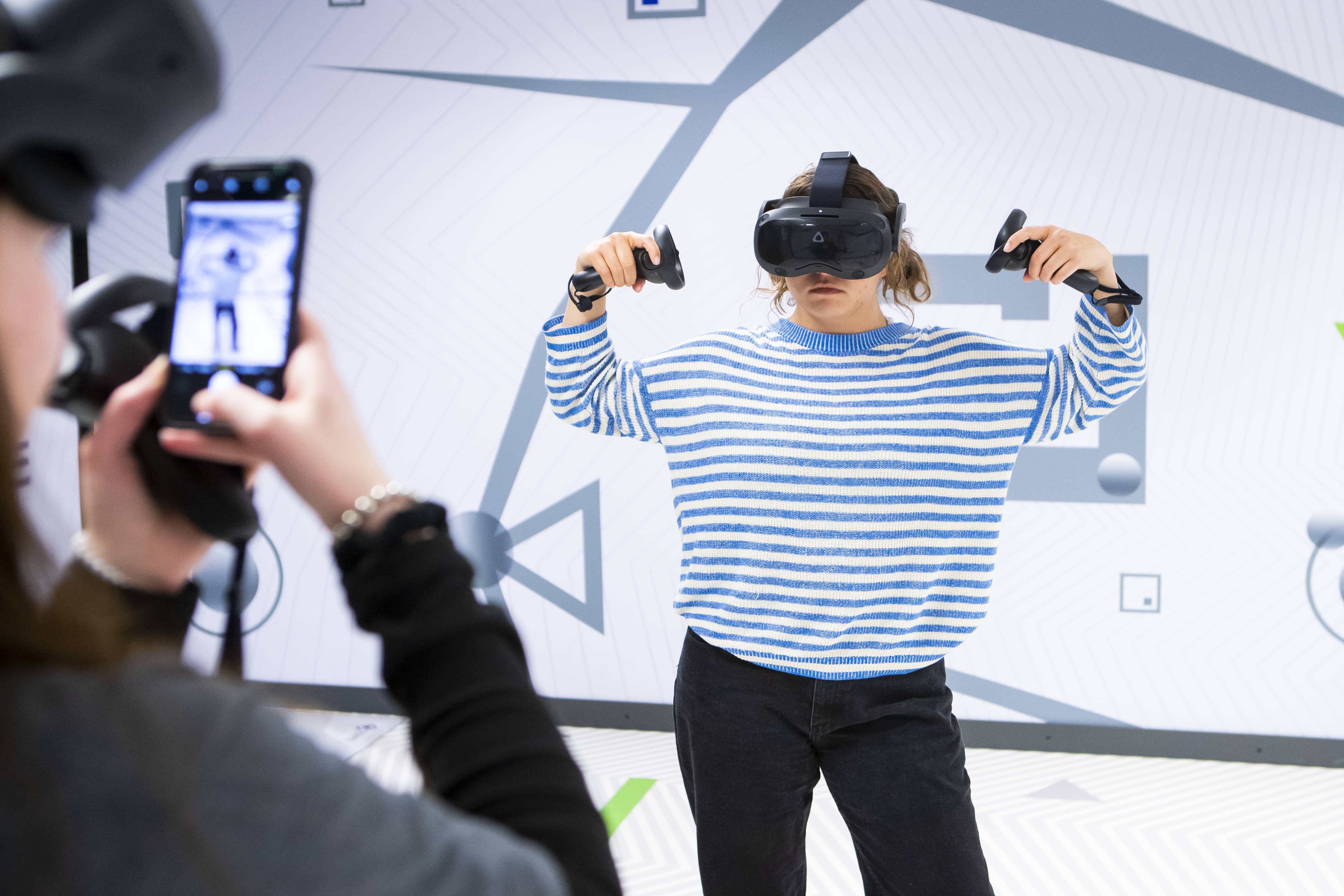 Student flexing for friend to take photo while wearing VR equipment.