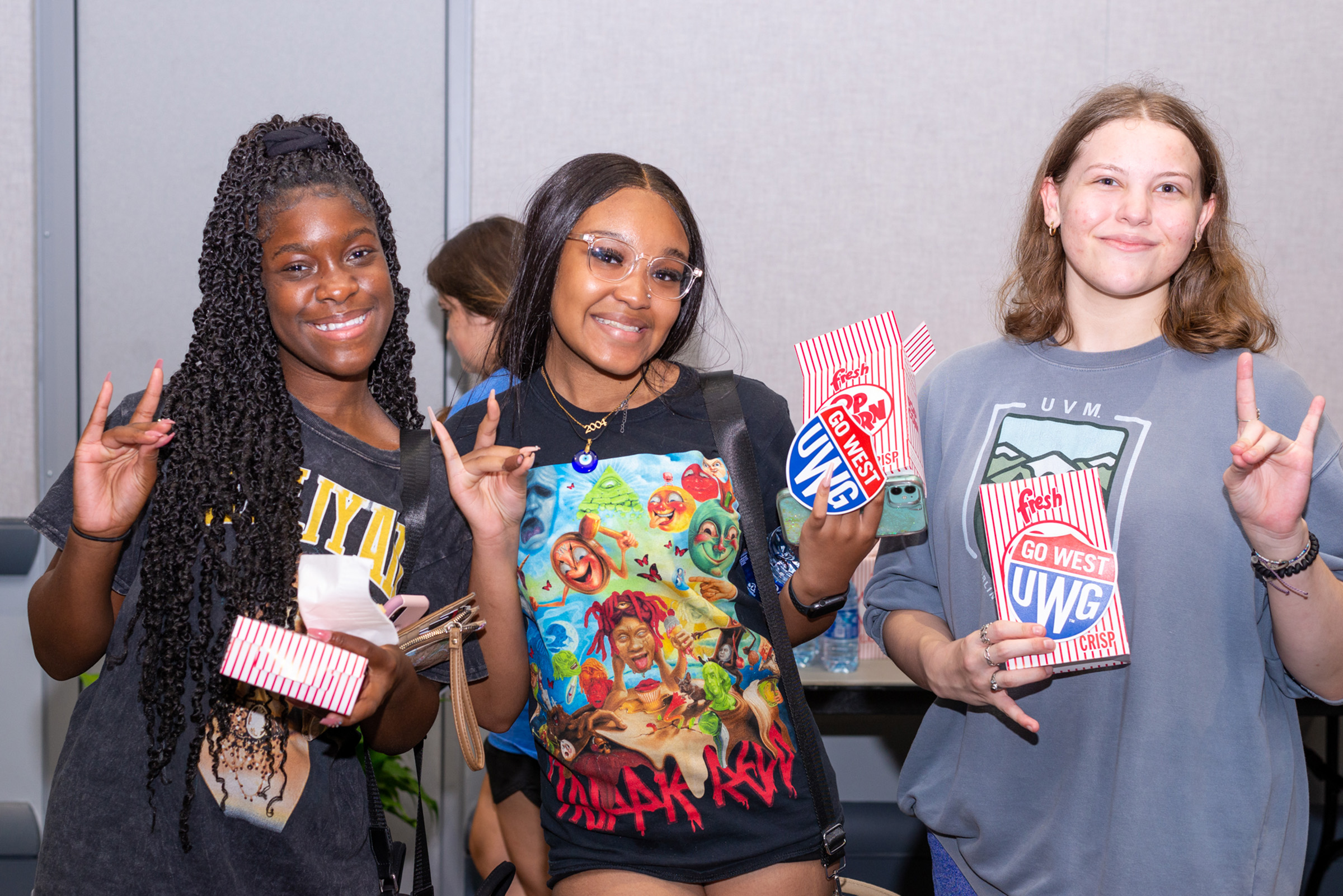 Students at Screen on the Green holding popcorn, UWG shield swag, and holding up the wolf hand sign