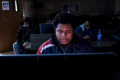 A male UWG student plays a computer game while two other males look on