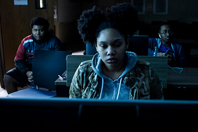 A female UWG student plays a computer game while two male students look on