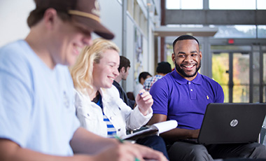A guy laughing with friends while working on a laptop