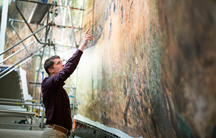 Photo of University of West Georgia graduate Jesse Garbowski pointing up at the Battle of Atlanta Cyclorama painting.