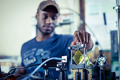 A UWG student in a baseball cap taking physical measurements in a lab