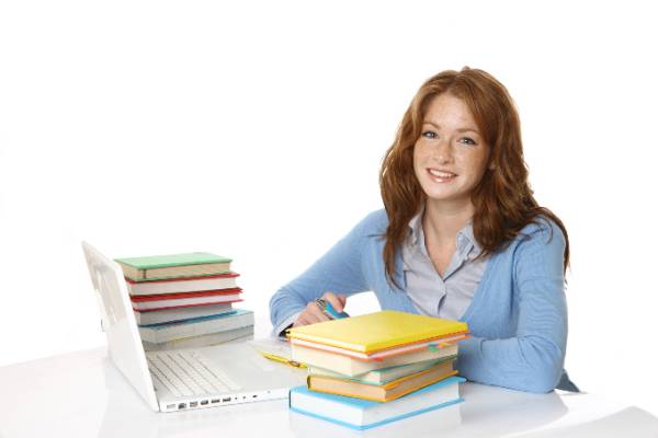 Female dual enrollment student sitting at a desk with her laptop and a stack of books.