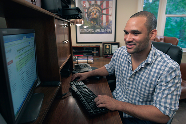 Man in blue button down sitting at his desk working on his computer.